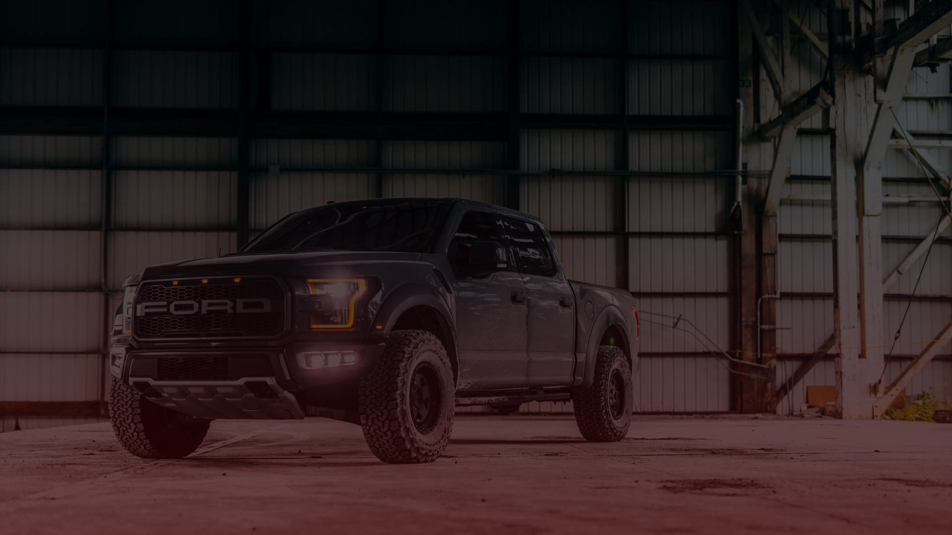 A rugged Ford pickup truck with off-road tires and a prominent grille is parked inside a spacious, industrial warehouse in Toronto. Its headlights illuminate part of the large, empty concrete floor as if waiting for a skilled mechanic to begin an adventure. EuroMechanic | McDermott Motors Auto | Top Reviewed Auto Repair Shop in Toronto | Visit mcdermottmotors.com