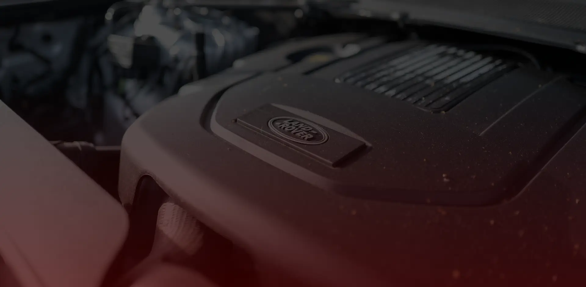 Close-up view of a Land Rover car engine, showcasing the logo prominently on a sleek black engine cover. The lighting highlights the contours and texture, set against a blurred background of engine components, as if captured by a skilled Land Rover mechanic in Toronto. EuroMechanic | McDermott Motors Auto | Top Reviewed Auto Repair Shop in Toronto | Visit mcdermottmotors.com
