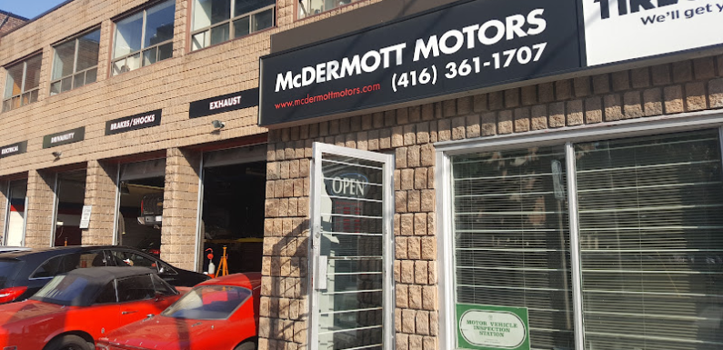 Exterior of McDermott Motors, showing a brick building with garage doors labeled for different services like exhaust and brakes. A red car is parked nearby. A sign displays the phone number and the word OPEN on a door. EuroMechanic | McDermott Motors Auto | Top Reviewed Auto Repair Shop in Toronto | Visit mcdermottmotors.com