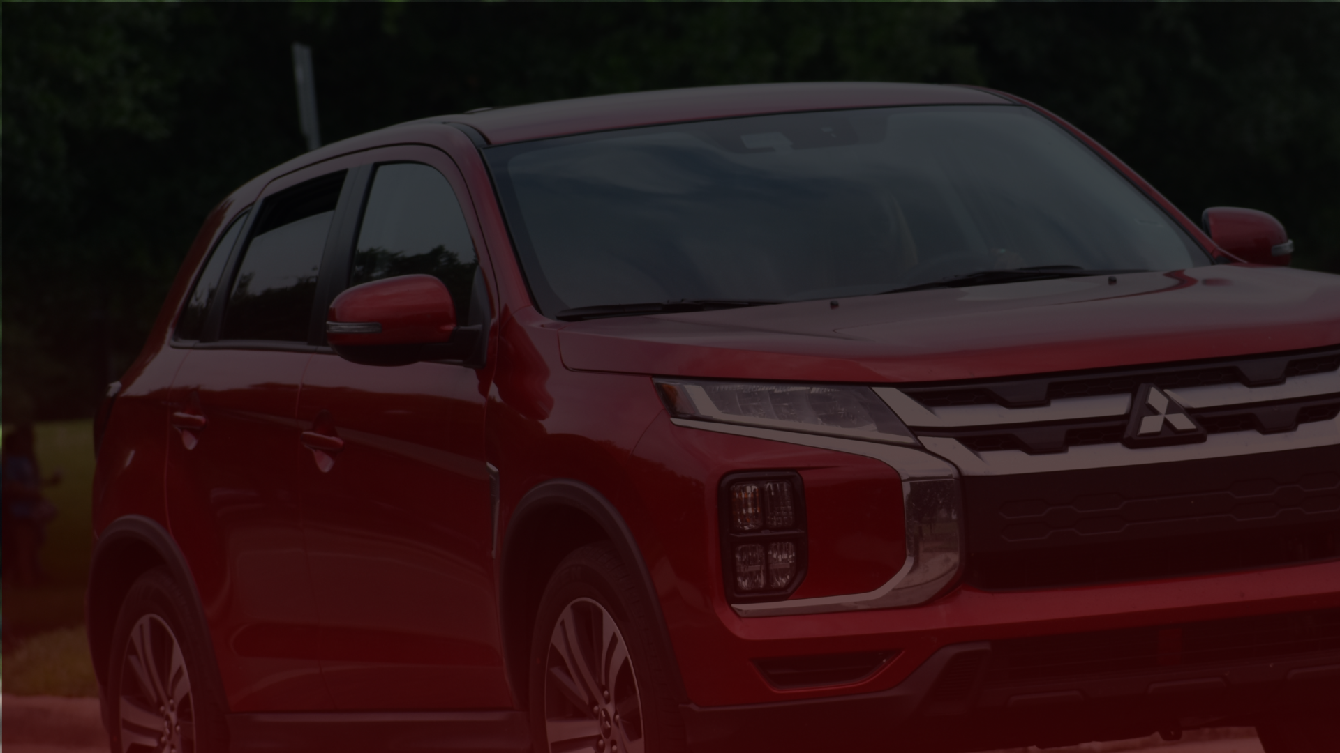A red Mitsubishi SUV, expertly maintained by a top Toronto mechanic, is parked outdoors against a blurred grassy background. The vehicle showcases a sleek, modern design with distinct headlights and a prominent front grille. EuroMechanic | McDermott Motors Auto | Top Reviewed Auto Repair Shop in Toronto | Visit mcdermottmotors.com