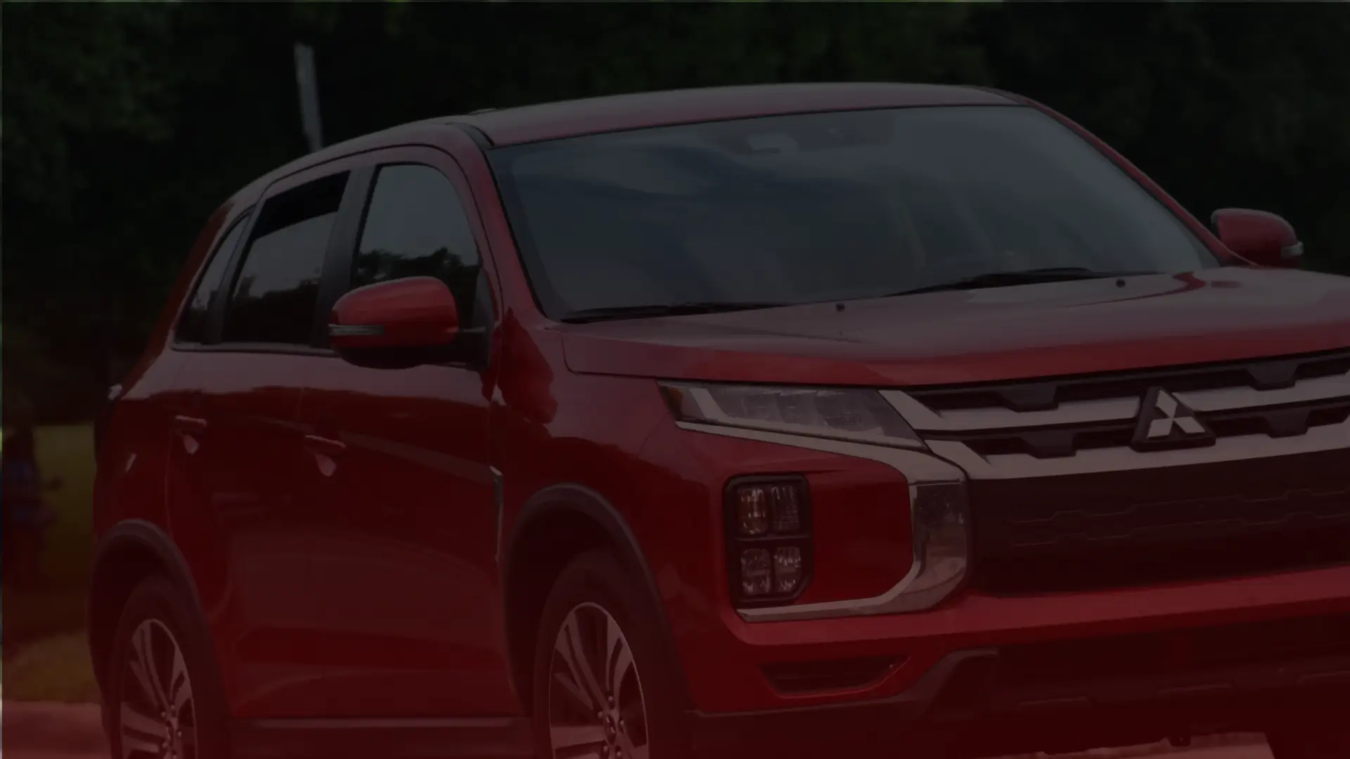 A red Mitsubishi SUV, expertly maintained by a top Toronto mechanic, is parked outdoors against a blurred grassy background. The vehicle showcases a sleek, modern design with distinct headlights and a prominent front grille. EuroMechanic | McDermott Motors Auto | Top Reviewed Auto Repair Shop in Toronto | Visit mcdermottmotors.com