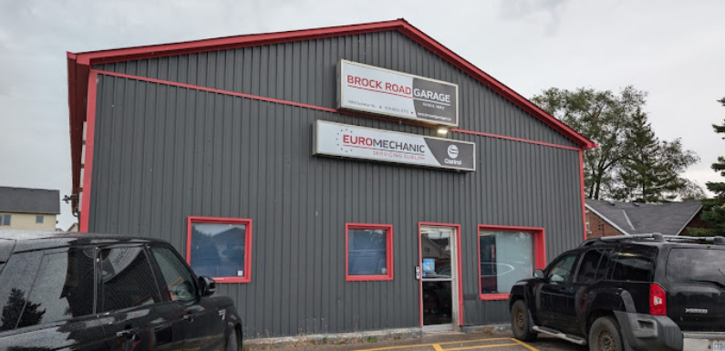 A grey building with red trim houses a garage named Brock Road Garage with additional signs for Euromechanic and Castrol. Two black vehicles are parked in front, and two small windows are visible on the left side of the entrance. EuroMechanic | McDermott Motors Auto | Top Reviewed Auto Repair Shop in Toronto | Visit mcdermottmotors.com