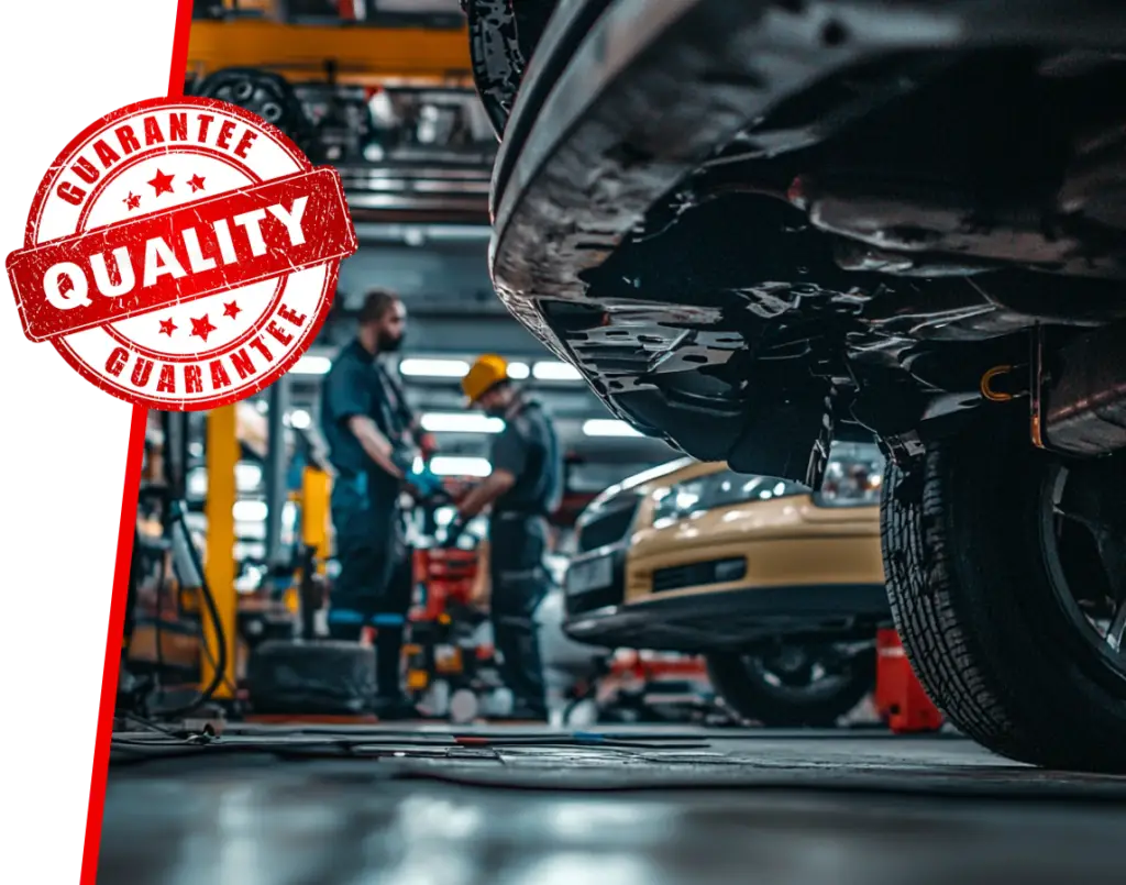 Close-up of a cars undercarriage in a Toronto garage. Two mechanics diligently work in the background, surrounded by various tools and equipment. A large red Quality Guarantee stamp assures top-notch auto repair prominently in the upper left corner. EuroMechanic | McDermott Motors Auto | Top Reviewed Auto Repair Shop in Toronto | Visit mcdermottmotors.com