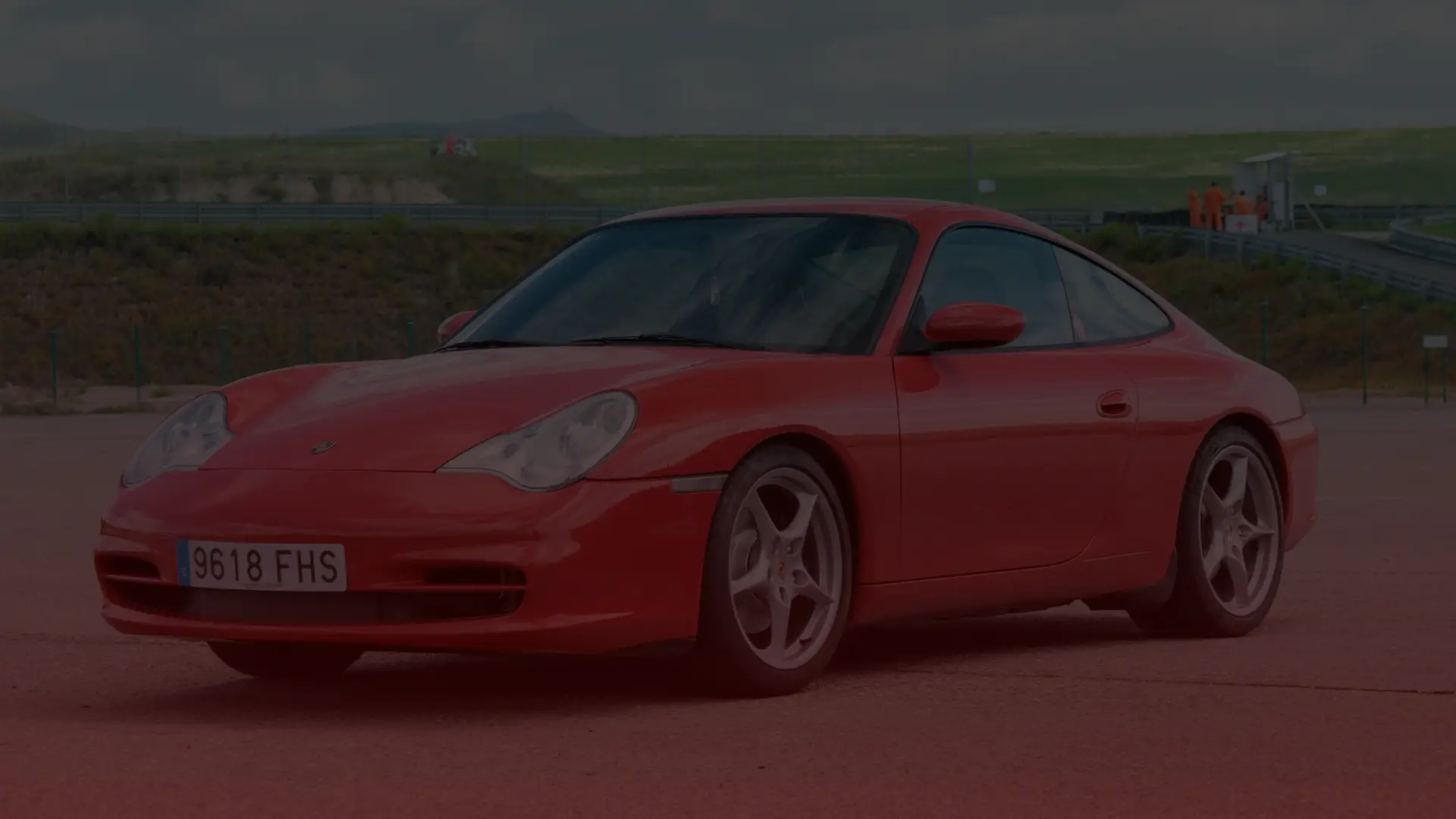 A red sports car is parked on an open paved area, its license plate reading 9618 FHS. Against a backdrop of grassy landscape and cloudy skies, this Porsche awaits attention from a skilled mechanic in Toronto. EuroMechanic | McDermott Motors Auto | Top Reviewed Auto Repair Shop in Toronto | Visit mcdermottmotors.com